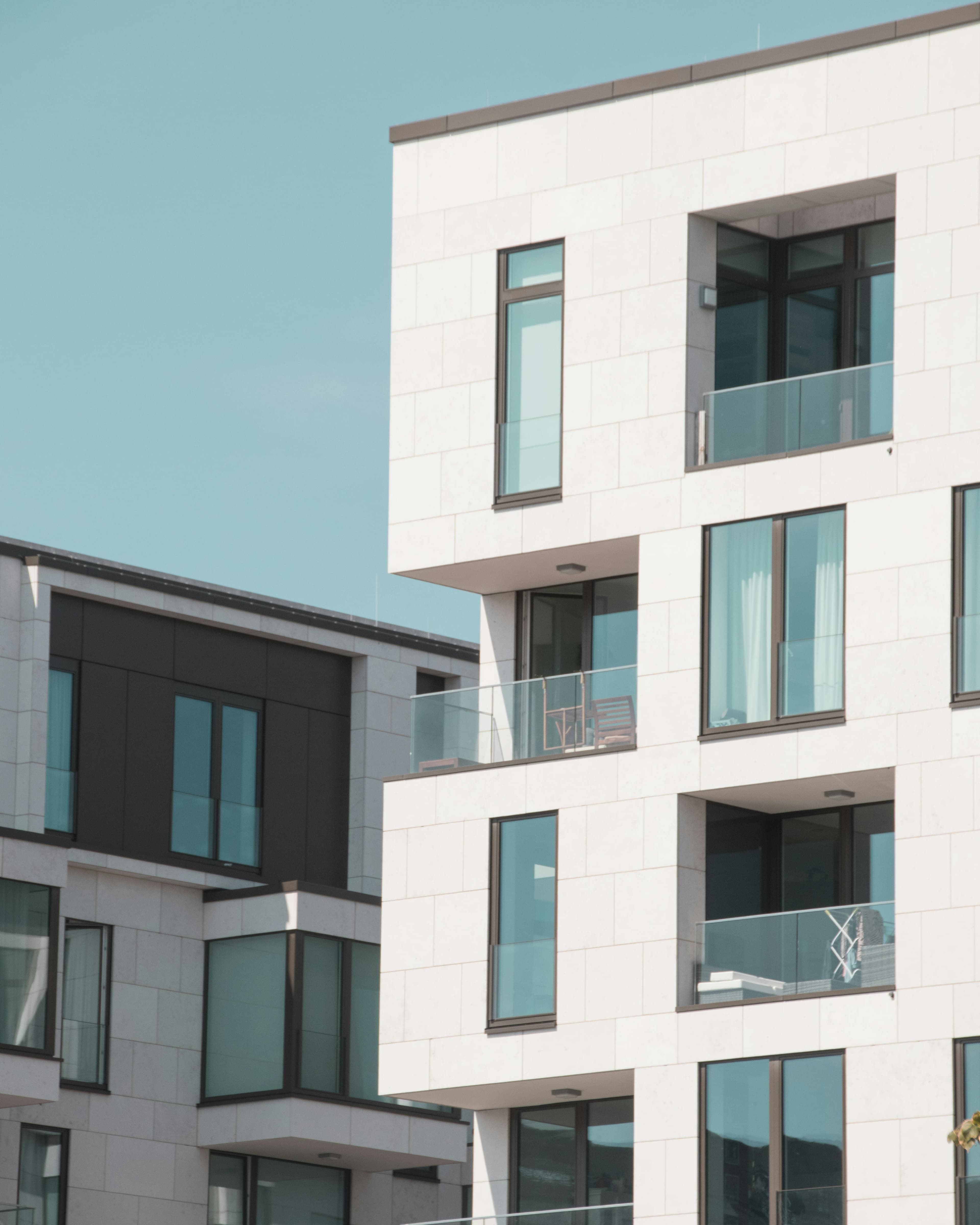 Moderne, weiße Wohnhausfassade mit Glasbalkonen – Neubau und Projektentwicklung im Bereich Residential.